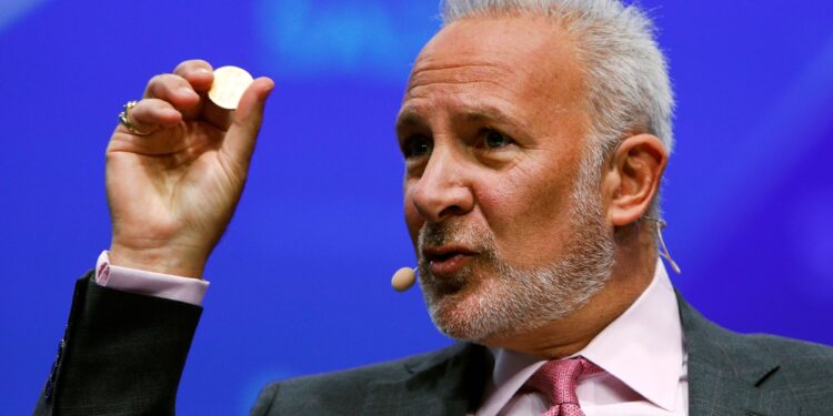 Peter Schiff aparace dando una conferencia y sostiene con su mano derecha una moneda física.