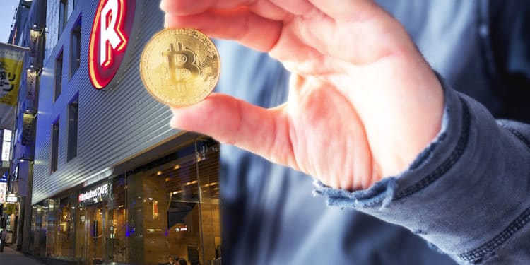 Mano de hombre con criptomoneda bitcoin afuera de tienda Rakuten.