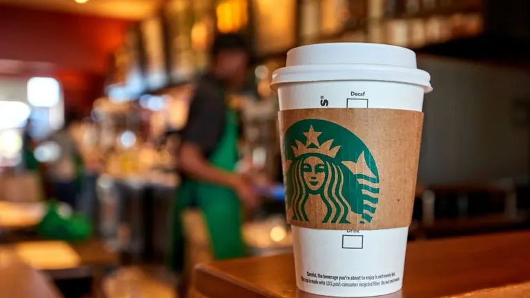 Vaso de Starbucks en una mesa con la cafetería y un empleado de fondo, imagen de archivo
