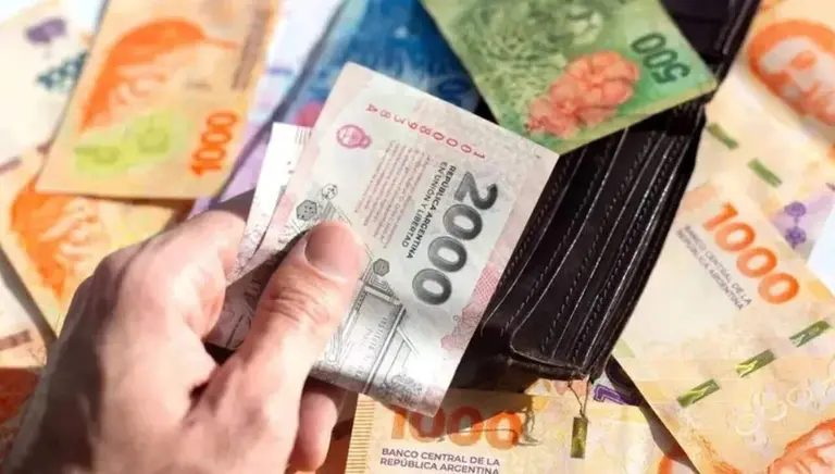 Mano sosteniendo un billete de 2.000 pesos sobre una billetera con un billete de 500 pesos y otros billetes de 1.000 pesos debajo. Imagen de archivo.